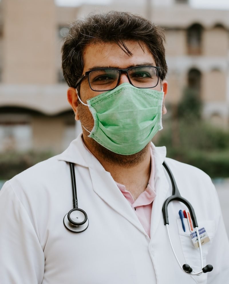 man in white scrub suit wearing green mask